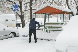 Person shoveling snow from a handicapped parking space near a park bench in winter.